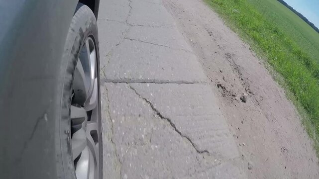 Close-up car wheel riding driving on damaged asphalt road in rural area.