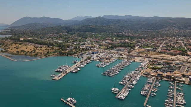 Aerial view of Lefkas Marina in Lefkada, Greece, featuring yachts, catamarans, turquoise water and mountain scenery on a sunny summer day.