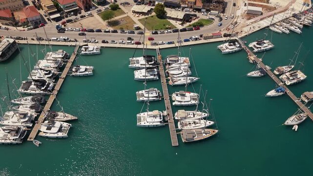 Aerial drone view of yachts and catamarans moored in Lefkada Marina, Greece, featuring turquoise water, marina docks and luxury boating lifestyle.