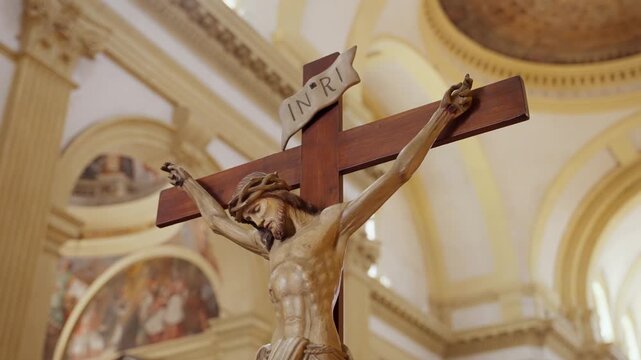 Wooden crucifix sculpture of Jesus Christ inside a church. Low angle view of the crucifixion figure with an INRI sign on top against a blurry religious interior background in European church in Italy