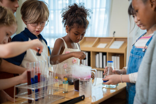 Diverse group of elementary school children focusing on chemistry experiment with smoke and test tubes in classroom. Students collaborating on science lab project with chemical reaction and dropper.