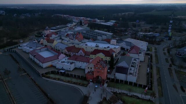 Outlet shopping center with empty parking lots, surrounding roads, roundabout and nearby railway infrastructure. Brilliant aerial view fly reverse panorama drone