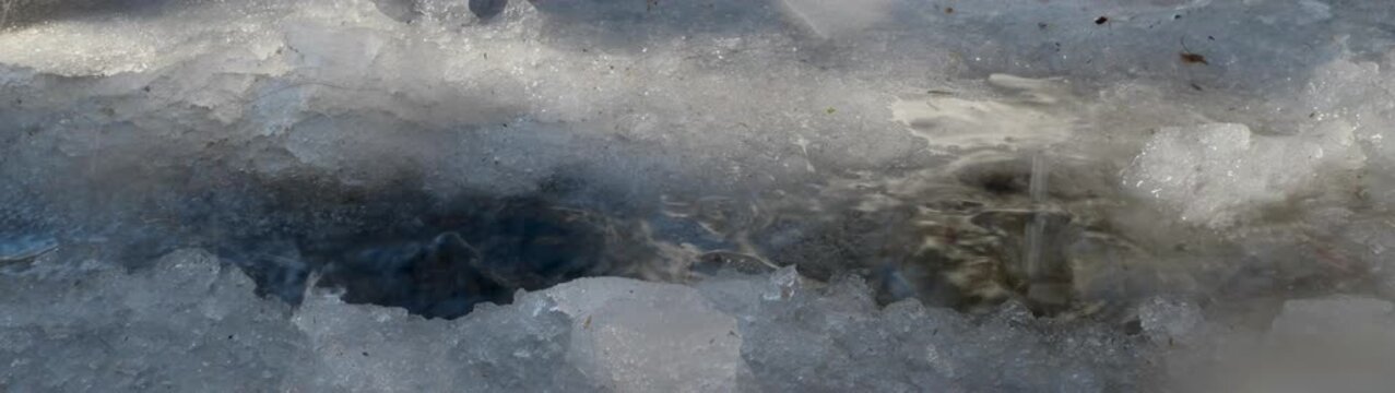 Melting ice and slush creating a small stream Gray and white tones reflect the cold winter conditions.