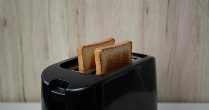 Toaster cooking bread slices in kitchen. Freshly toasted bread pops up from black toaster. Morning routine brings comfort and joy to breakfast.