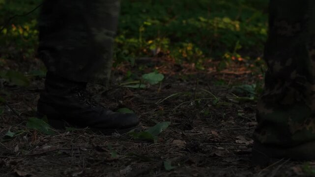 Three soldiers in camouflage walking across terrain in forest, legs close-up.
