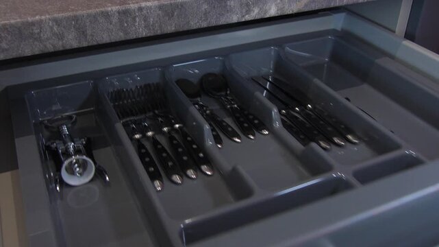 Modern kitchen drawer with tableware utensils and corkscrew inside.