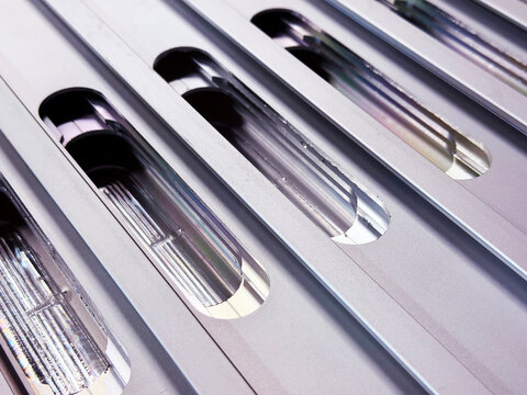 Precision machined aluminum profiles with elongated oval cutouts; close-up of industrial metal extrusion with slots for technical applications.