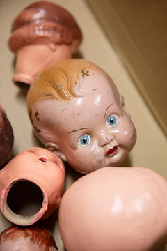 Collection of vintage doll heads scattered in a cardboard box, some with chipped paint