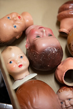 Collection of vintage doll heads scattered in a cardboard box, some with chipped paint