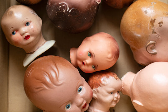 Collection of vintage doll heads scattered in a cardboard box, some with chipped paint