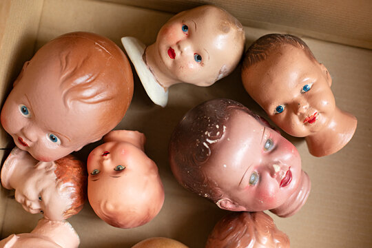 Collection of vintage doll heads scattered in a cardboard box, some with chipped paint
