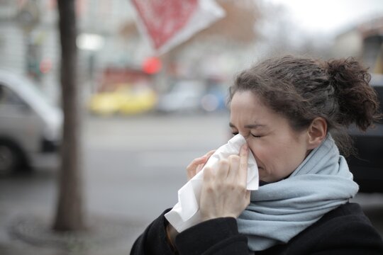 Sick woman blowing her nose with a tissue outside