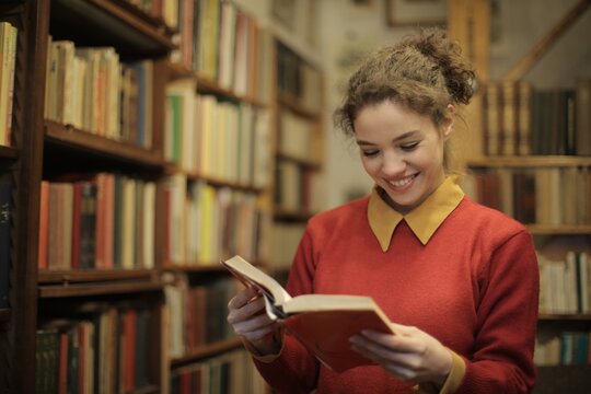 Happy young woman reading a book in library