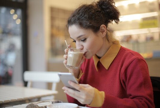 Young woman sipping coffee and using her smartphone