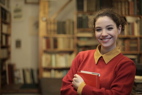 Cheerful female student holding a book in a library