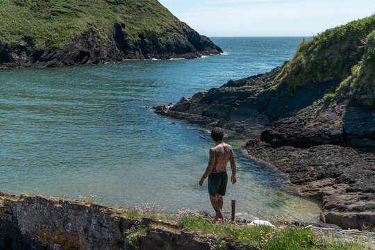 Man approaching calm blue water in rocky cove
