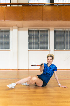 Smiling woman badminton player sitting on gym floor