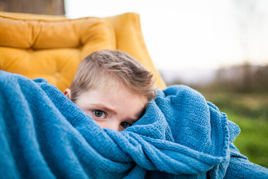 Shy young boy peeking over a blue blanket