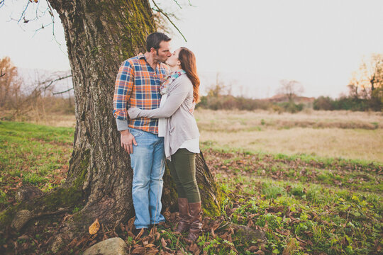 Romantic couple share a kiss outdoors by a tree