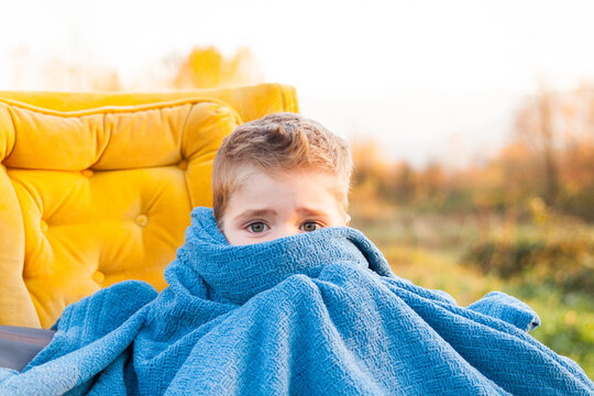 Worried little boy hiding face in a blue blanket