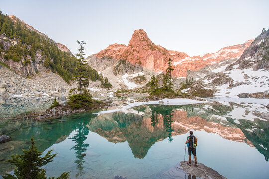 Hiker taking in a beautiful alpine lake mountain reflection