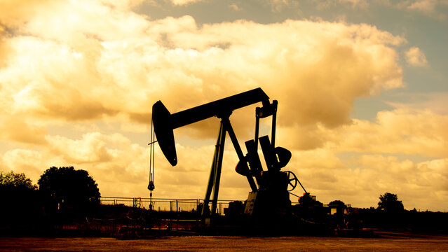 Chevalet de pompage en silhouette sur un arri&egrave;re plan de nuages au soleil couchant. Exploitation d'un puits de p&eacute;trole et extraction du p&eacute;trole brut. Concepts de prix du p&eacute;trole et crise &eacute;nerg&eacute;tique