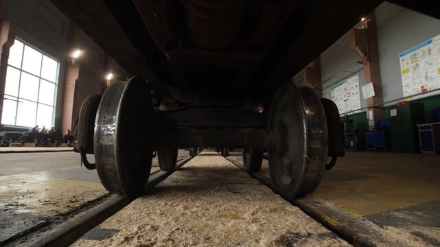 View from rails on bottom of cargo railway wagon in mining factory workshop.