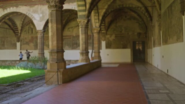 Blurred cloister with arched stone columns, tiled walkway and sunlit lawn in soft bokeh interior; background backplate copyspace calm.
