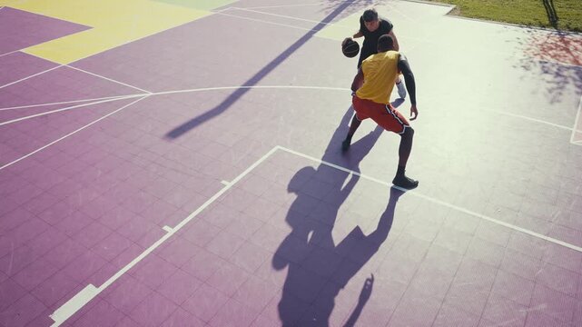 Two diverse men are intensely playing basketball on a vibrant purple outdoor court, with one player dunking the ball into the hoop while the other defends