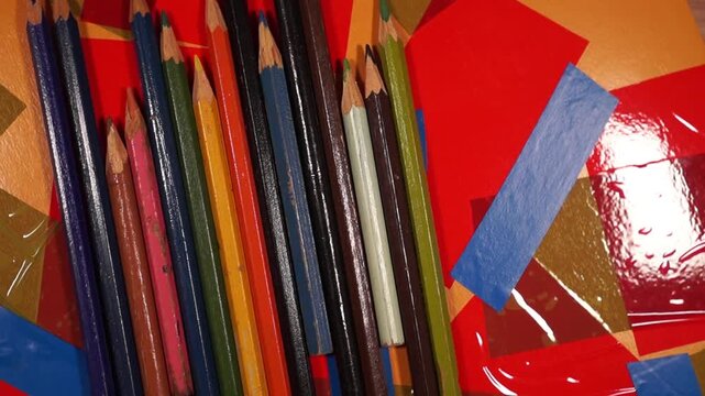 Rotation of pencils on colorful duct tape surface. Close-up, topview	
