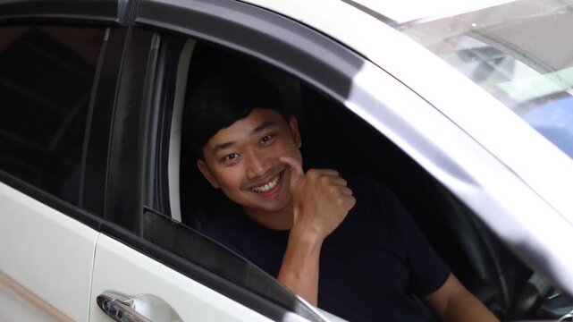Asian man in his car slide car mirror and look at camera with happy smile and thumb up