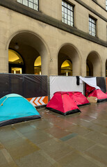 Tents and Homeless Encampment Outside Stone Arched Building in Urban Street Scene © © Raymond Orton