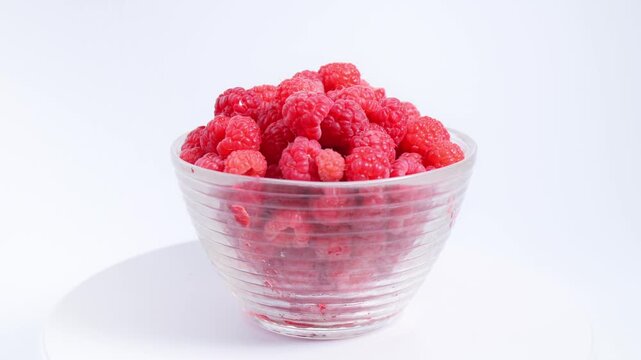 Fresh raspberries in glass bowl rotating on white background highlight raspberry freshness, vibrant berry quality, premium fruit presentation for food branding, retail packaging, healthy lifestyle