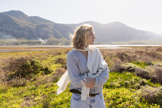 young stylish woman wearing scarf relaxing at resort overlooking Klein Mountains and Lagoon, Stanford, South Africa