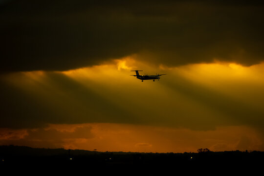 View of a propeller airplane silhouette flying through golden sunbeams and dark clouds at sunset near Jomo Kenyatta International Airport in Nairobi, Nairobi County, Kenya.