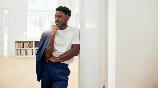 Contemplative Man in Suit, Leaning Against Wall with Hands in Pockets