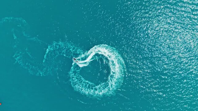 A watercraft moves quickly in bright blue waters creating a wave pattern as it turns. Sunlight reflects off the surface creating a vibrant scene at sea during daytime.