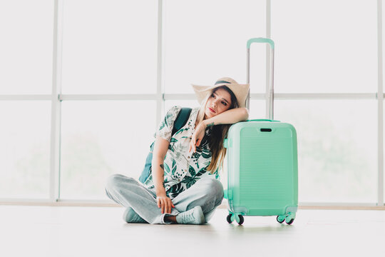 Sad woman leaning on suitcase in airport terminal, enjoying casual travel attire and tropical style for her journey