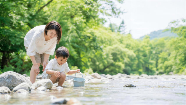 浅い川でバケツを使って川遊びをする日本人親子