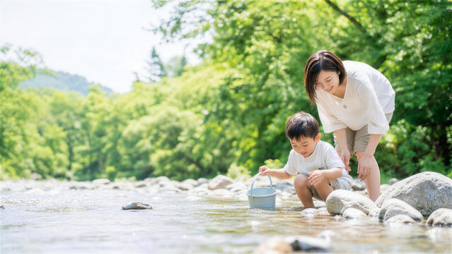 浅い川でバケツを使って川遊びをする日本人親子