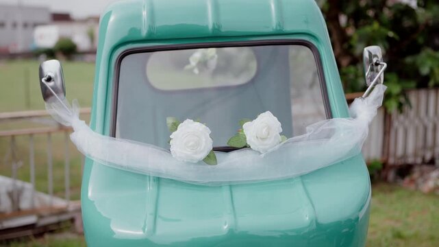 Front hood of vintage turquoise car decorated with white roses and white tulle for wedding