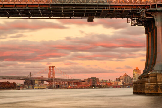 Manhattan Bridge frames the Williamsburg Bridge over the East River at sunset, showcasing urban tourism and travel exploration in New York City, Manhattan Bridge, Williamsburg Bridge.