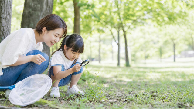 公園で虫眼鏡を使って昆虫観察をする日本人親子