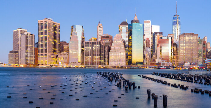 Lower Manhattan skyline and illuminated skyscrapers overlook the East River waterfront at twilight, highlighting a classic New York City tourism destination.