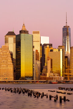 Lower Manhattan skyline reflects golden sunset light over East River wooden pilings, capturing an iconic urban tourism destination, New York City, USA.
