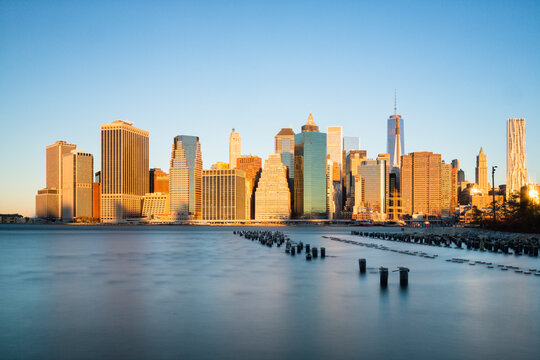 Manhattan skyline skyscrapers rise above the calm East River during golden hour, capturing an iconic urban tourism destination in Lower Manhattan, New York City, USA.