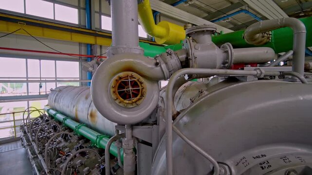 Close up of large industrial diesel engine with turbocharger red impeller cylinders exhaust manifold and green pipework inside power plant machine hall