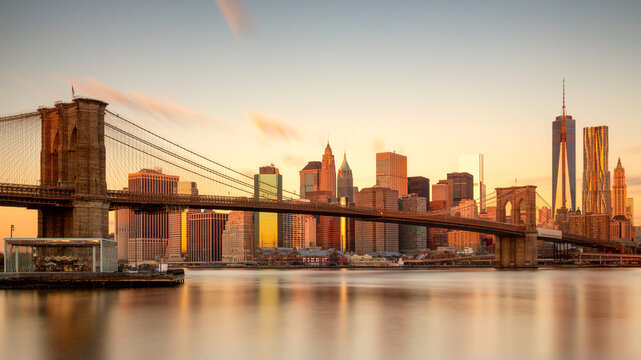 Brooklyn Bridge and the iconic Lower Manhattan skyline glow during a golden hour sunset over the East River, capturing the essence of urban tourism in New York City.