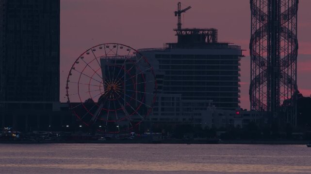 View of city embankment with illuminated Ferris wheel at sunset in Batumi.