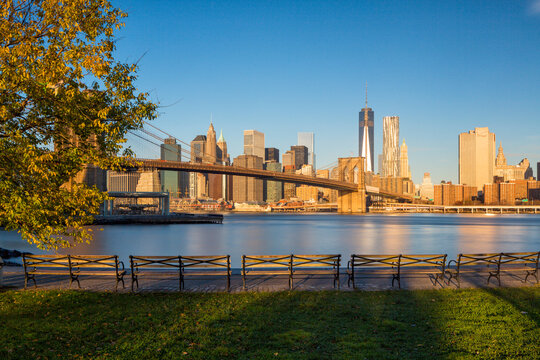 Brooklyn Bridge and Lower Manhattan skyline viewed from an empty park waterfront, featuring autumn foliage and copy space for urban tourism and travel advertising, New York City, USA.